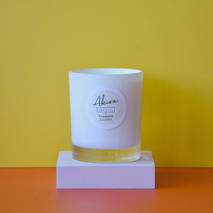 Yellow wall, orange floor. A white Akira Grateful natural soy wax candle on a pink podium.