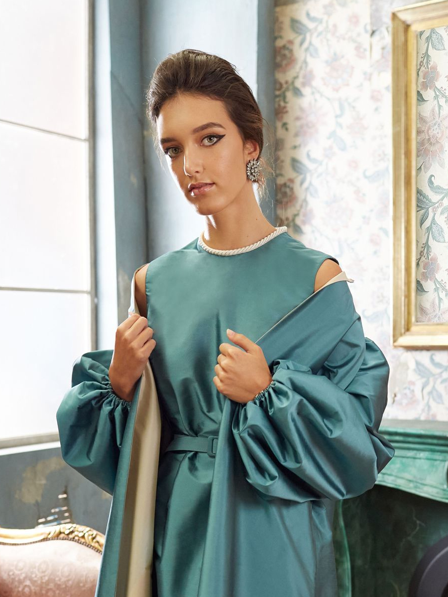 Woman in a teal dress and belt, with a matching coat,