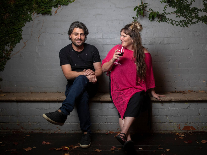 a man in a black top and woman in pink kaftan holding a glass of wine