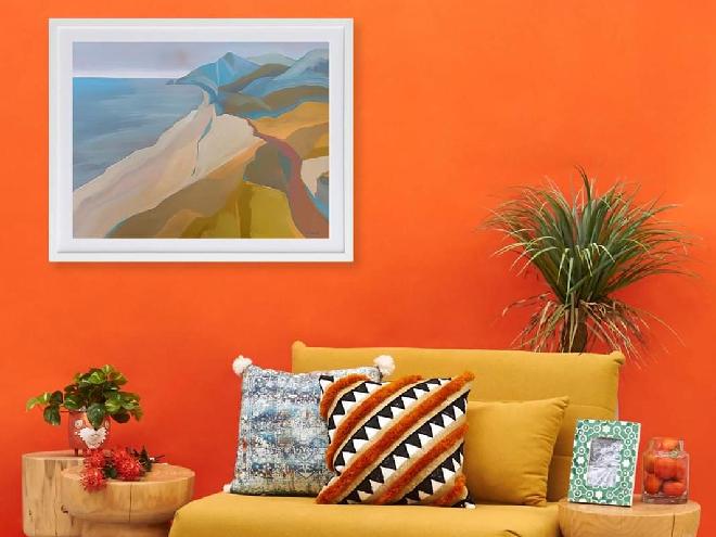 Orange painted walls with framed photo of the coast, a yellow seat and patterned throw cushions