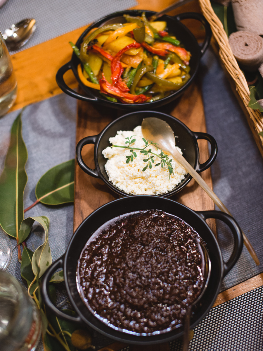 Three dishes including rice and vegetables on a wooden platter sitting on a table with a blue cloth and eucalyptus