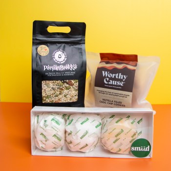 Yellow and orange background, a Persian brekkie pouch, a pack of Worthy Cause cookies and a pack of 3 Smeed Maamouls (semolina cookies) are in a box.